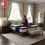 Person seated on an UltraFlex TruFirm mattress in a neutral bedroom.