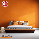 Low bed with grey bedding and gold cushions against a sunlit orange wall.