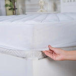 Hand lifting the elasticated edge of a white fitted mattress protector.